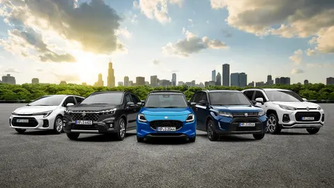 Aktuelle Suzuki Angebote - Bild verschiedener aktueller Suzuki-Modelle auf einem Parkplatz vor der Skyline einer Großstadt